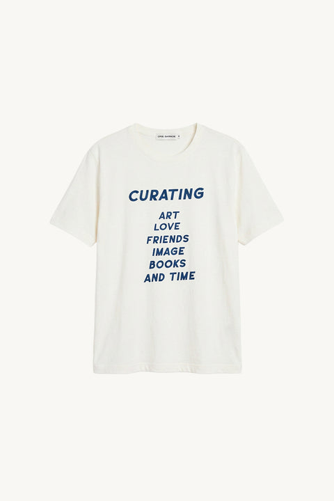 Camiseta branca da parceria cris barros e act arte, mostrando a parte da frente, escrito curating, art, love, friends, image, books and time